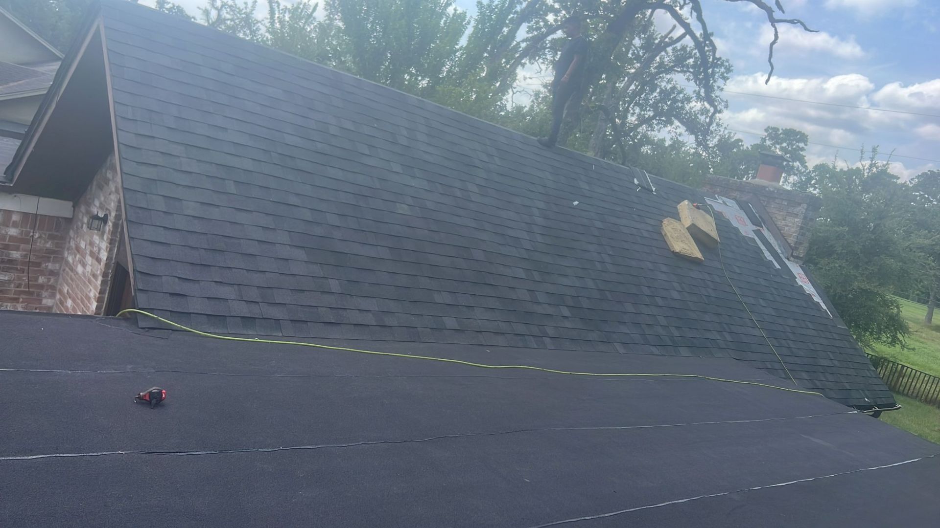 Black shingled roof with a missing section; a chimney and trees are visible in the background.