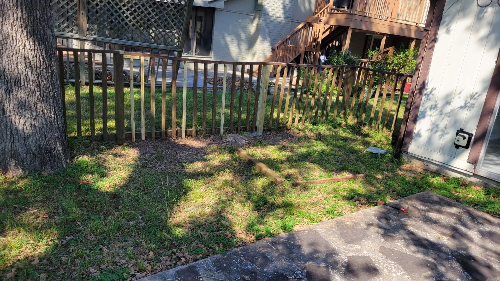 A grassy yard with a wooden fence next to a tree and a building.