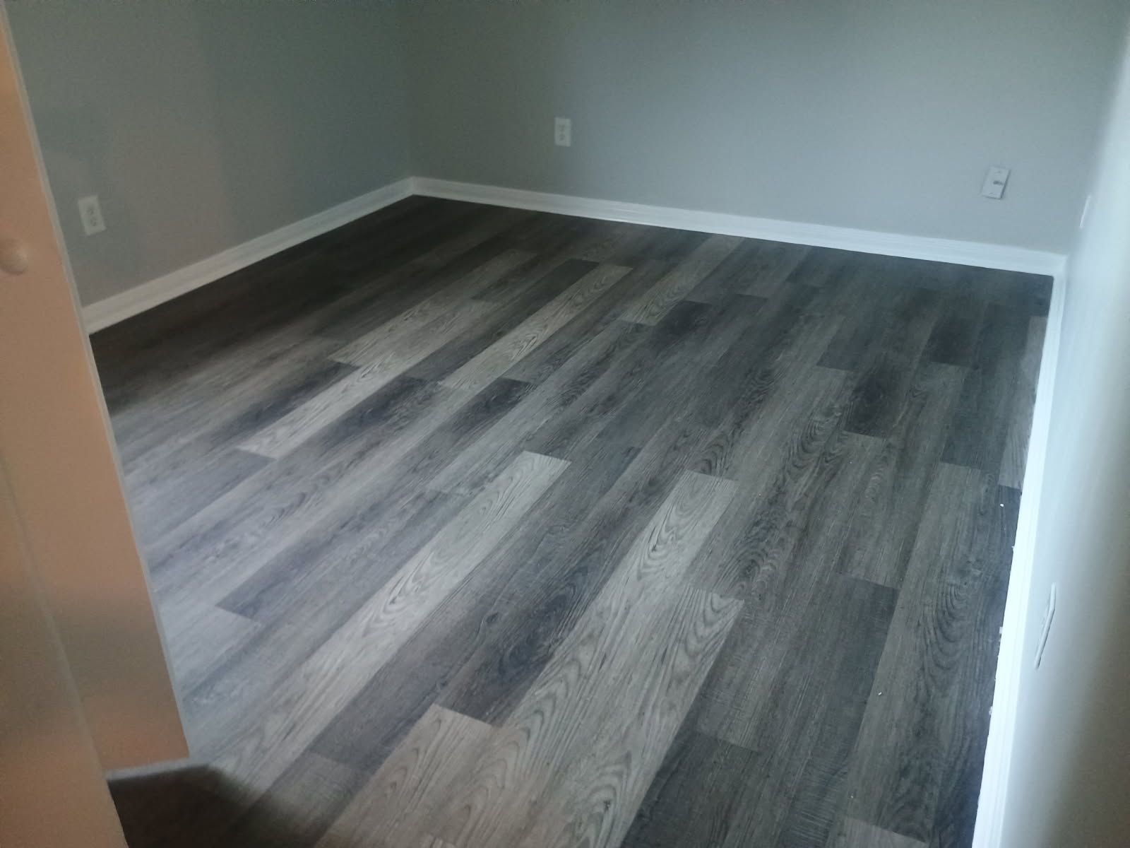 Empty room with gray wood-look flooring and white baseboards, gray walls.