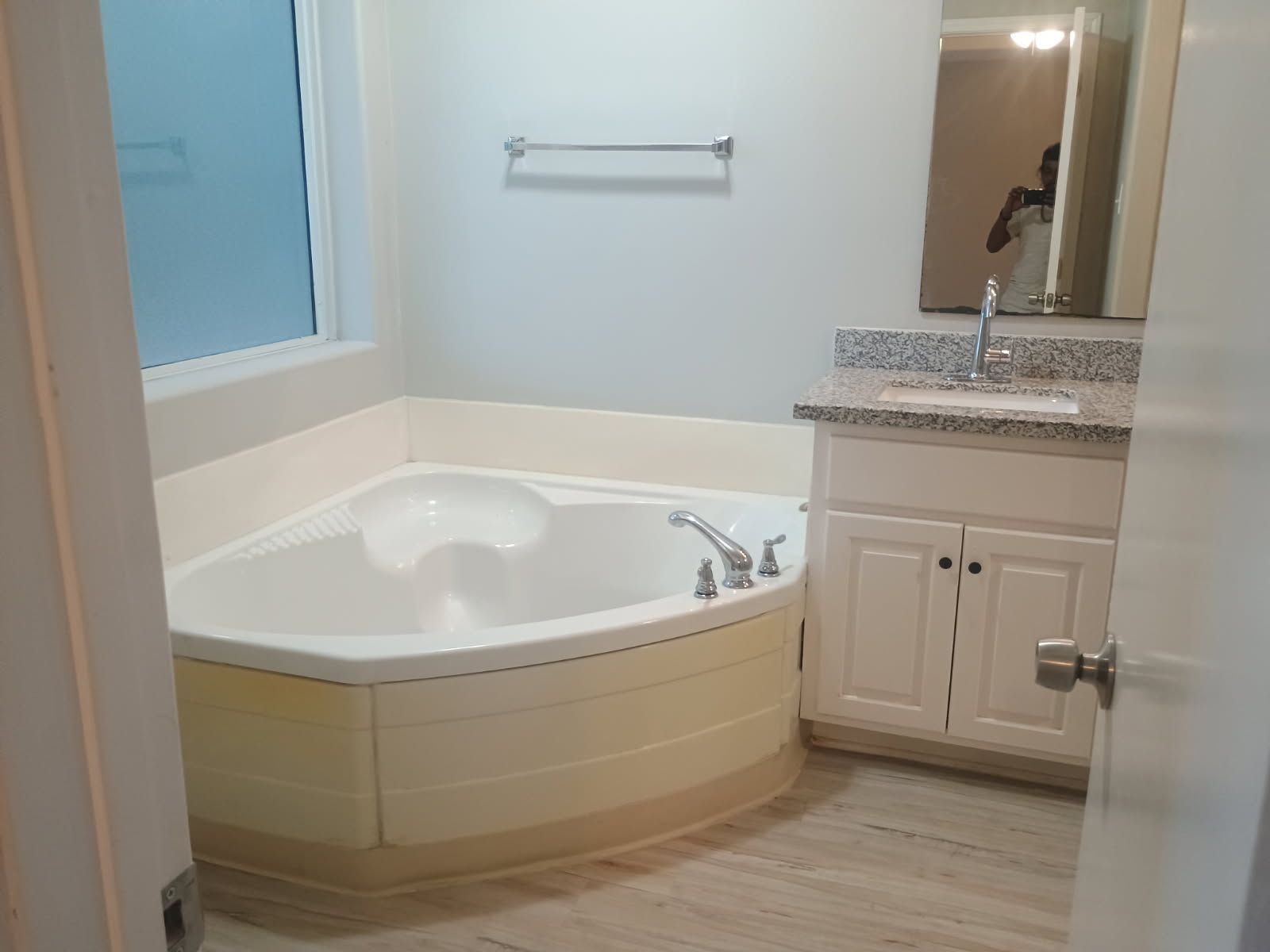 Bathroom with corner tub, white vanity, and frosted window. Beige and white tones dominate.