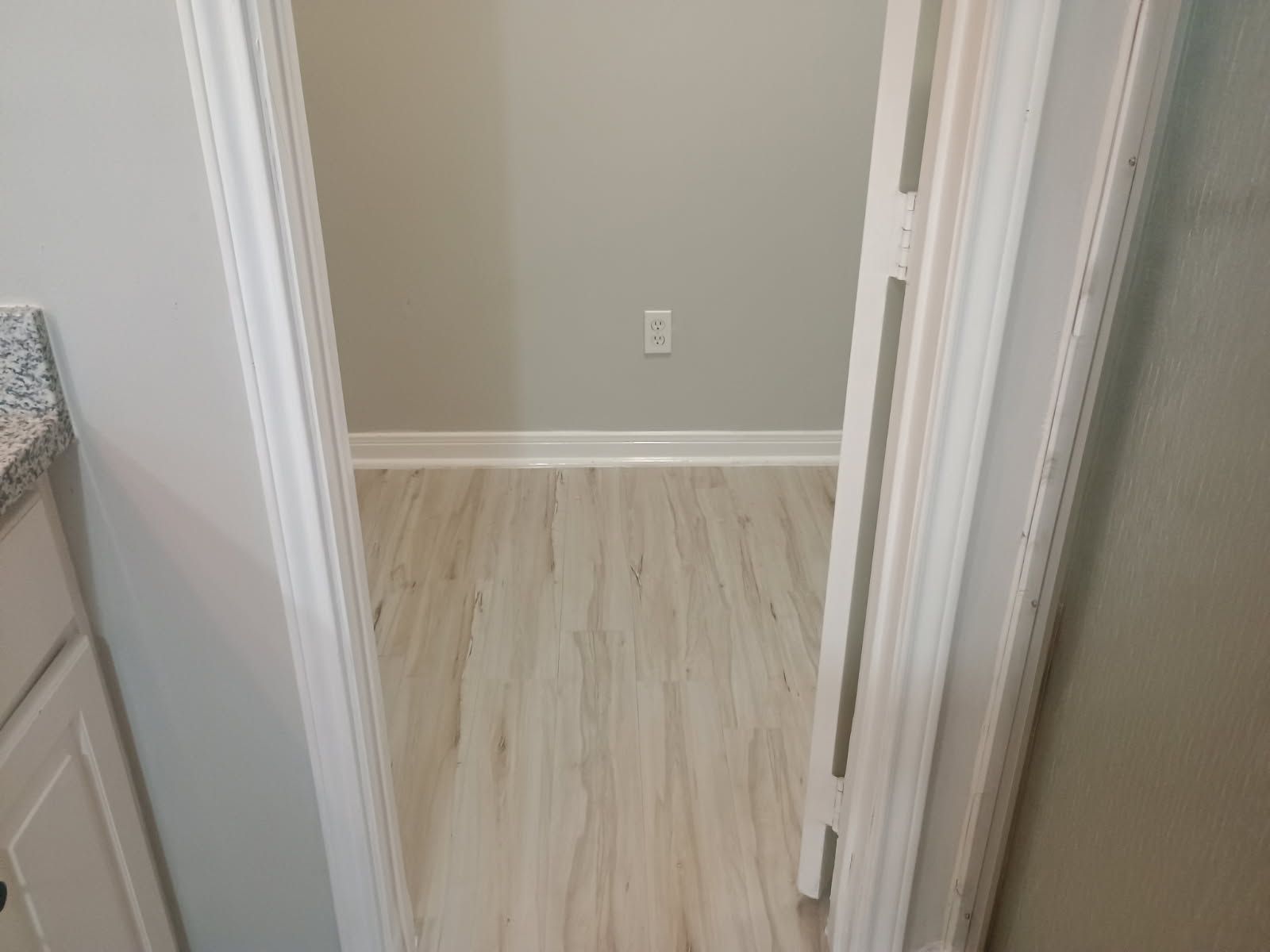 An open doorway leads to a small room with light wood-look flooring and gray walls.