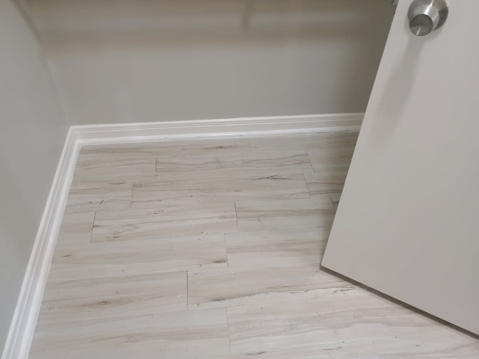 Light-colored tiled floor with door and white baseboard.