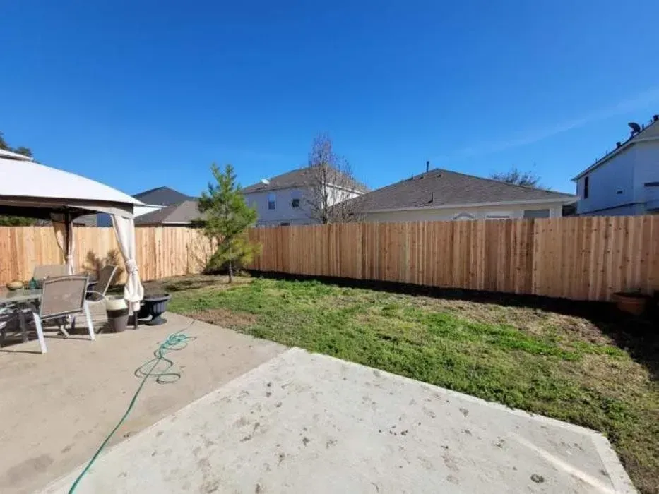Backyard with wooden fence, gazebo, patio, and patchy grass under a blue sky.