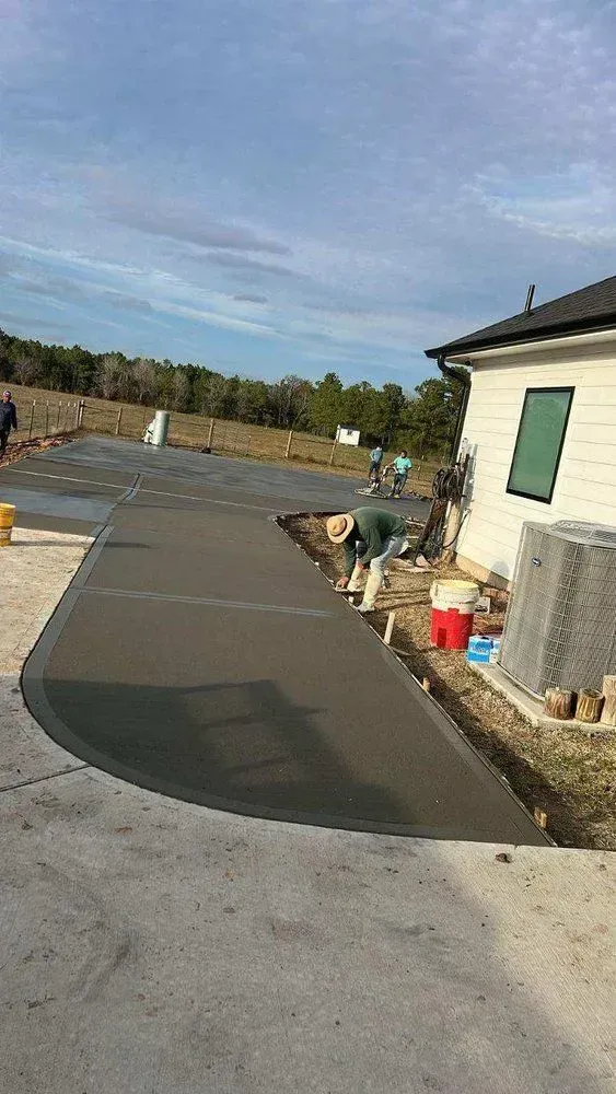 Workers pouring concrete for a driveway next to a white house under a cloudy sky.