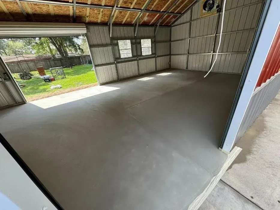 Interior of a garage with a freshly poured concrete floor. The garage door is open to a grassy yard.