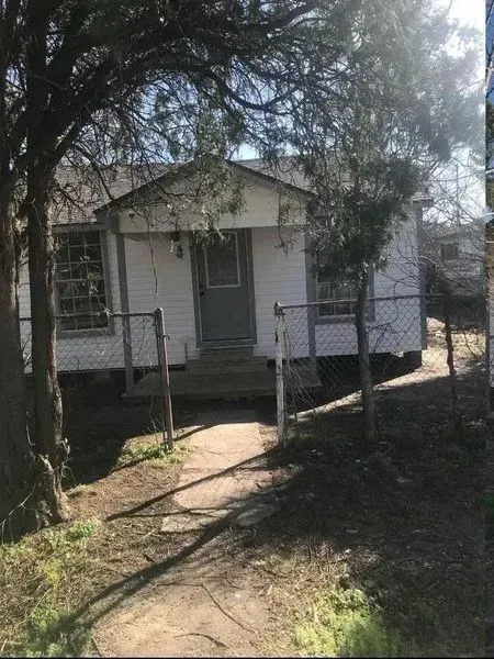 Small white house with a gray door, chain-link fence, and a stone path leading to the entrance.