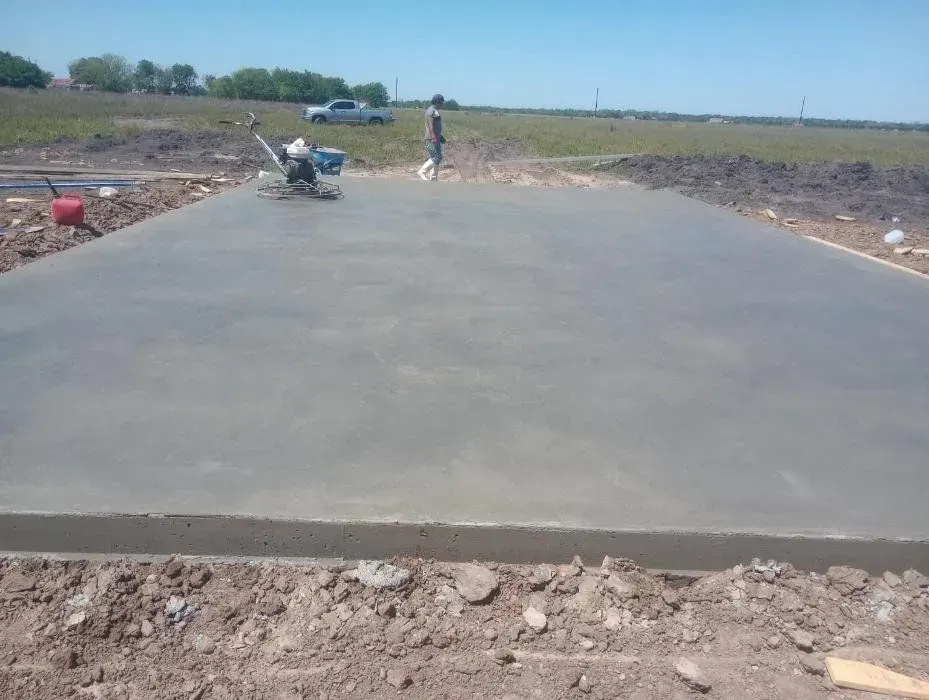 Newly poured concrete slab; worker using power trowel; outdoor construction site.