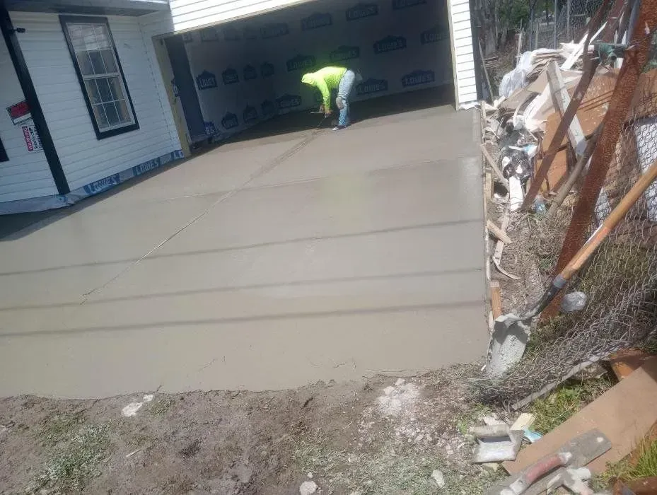 Worker smoothing wet concrete driveway in front of a garage.