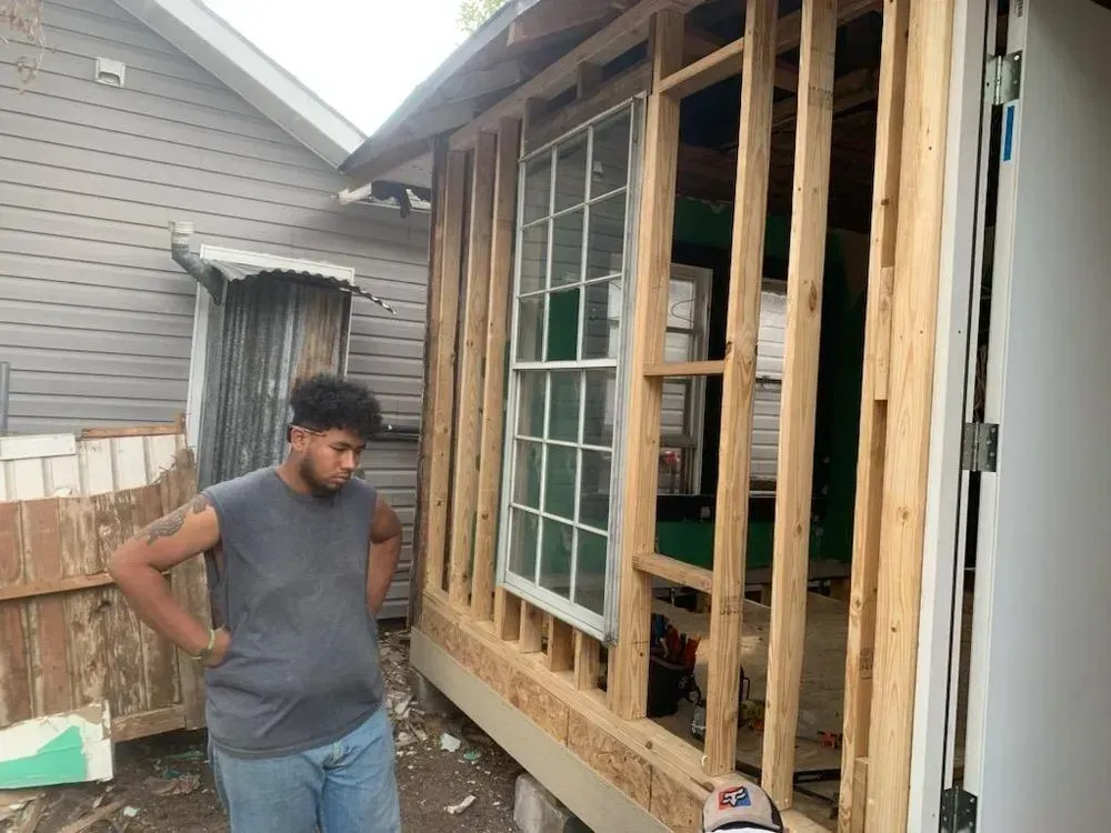 Person in gray tank top stands near a building under construction, looking at the work.