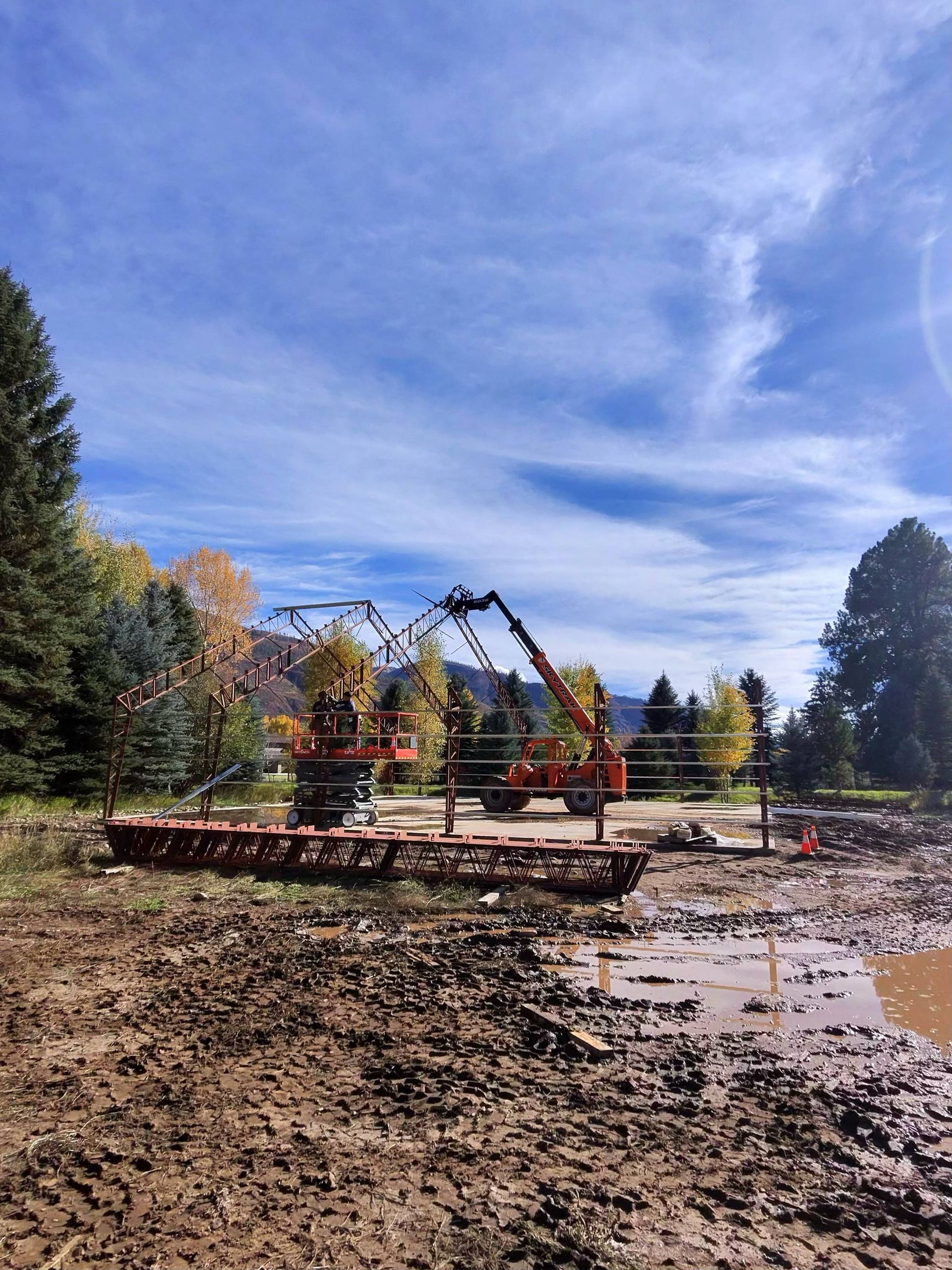 Construction site with mud, orange concrete pump trucks, and blue sky.
