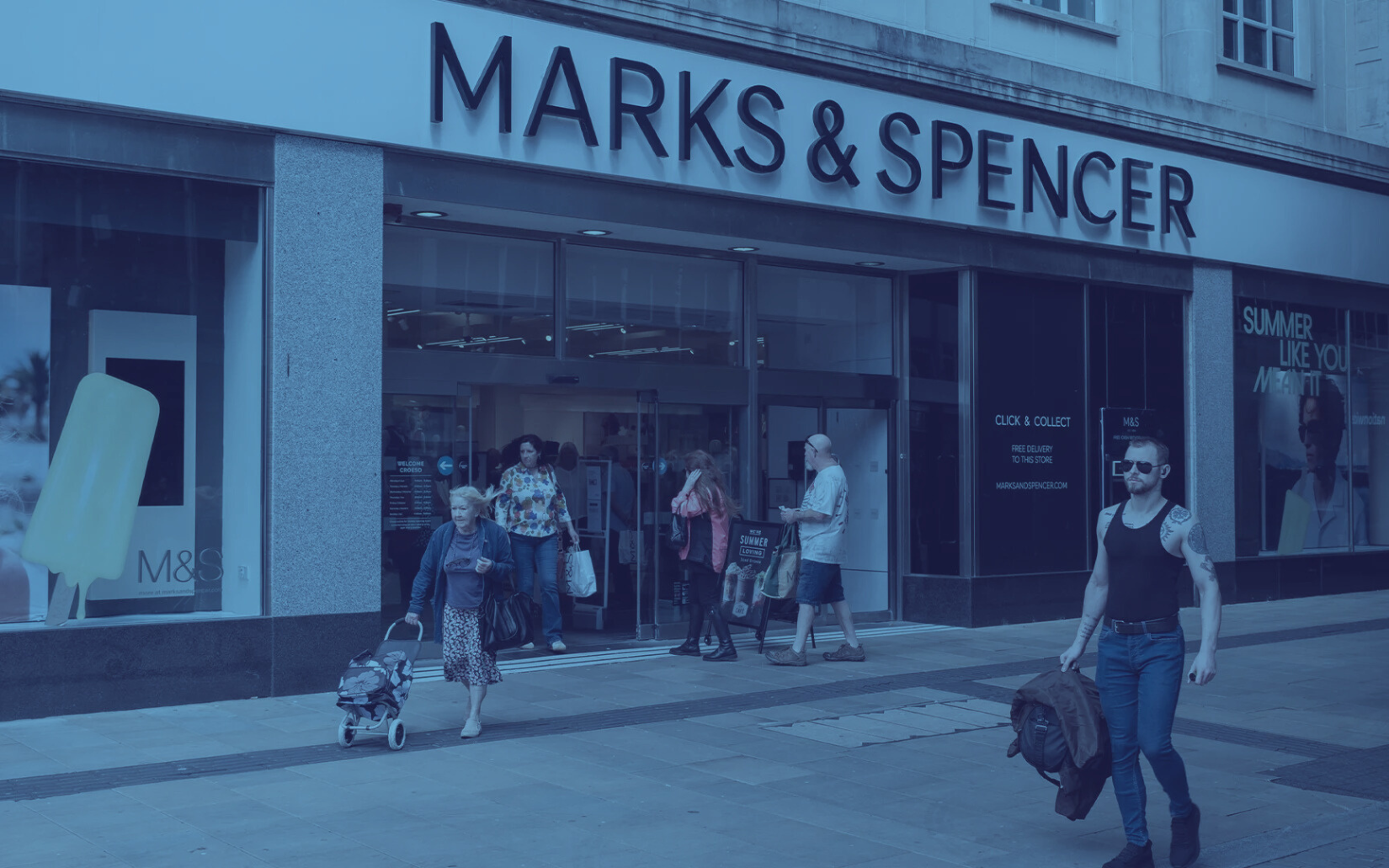 A group of people are walking down a street in front of a marks & spencer store.