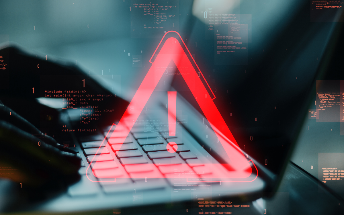 A person is typing on a laptop with a red warning sign on the keyboard.