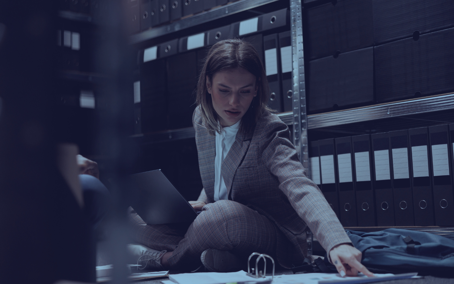 A woman is sitting on the floor in a dark room looking at a laptop.