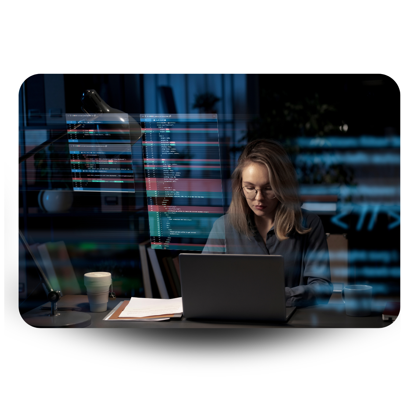 A woman with glasses working on a laptop at night, code displayed on screens in the background, and a lamp on the desk.