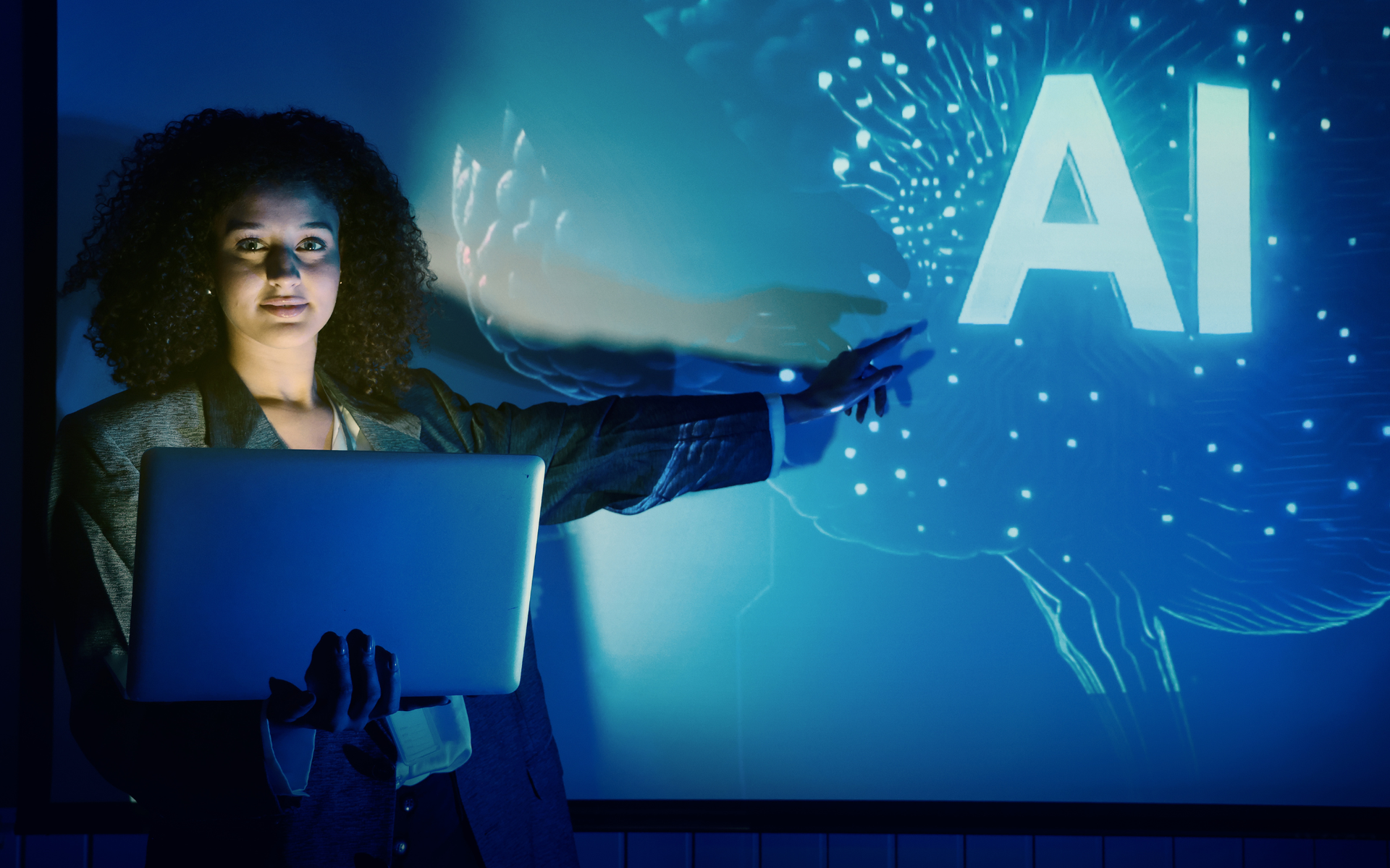 Woman presenting AI concept on screen, pointing with a laptop. Blue tones, glowing 