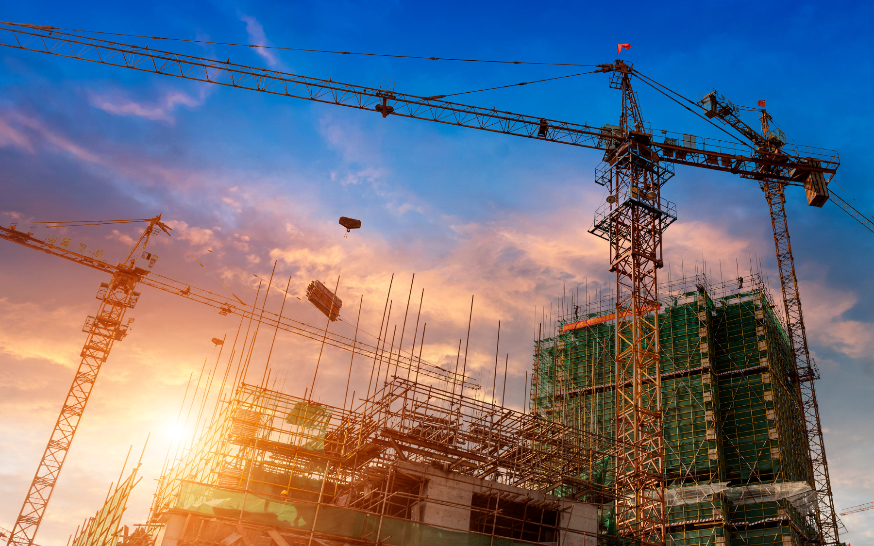 Construction site with cranes silhouetted against a sunset.