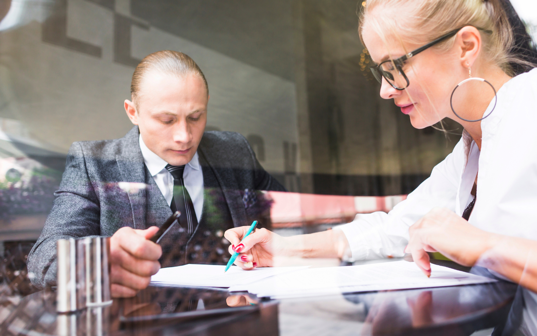 Man and woman in business attire reviewing documents at a table; light streams through a window.