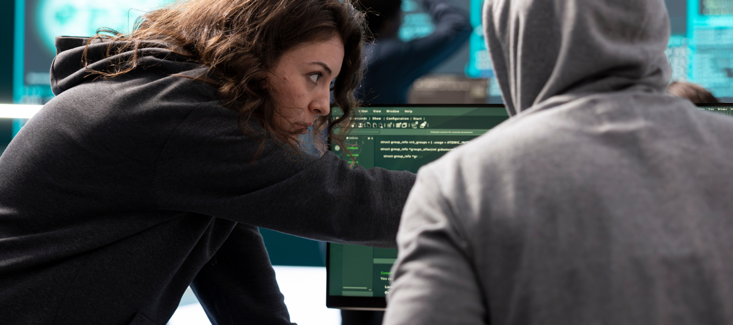 A woman in a hoodie is standing next to a man in a hoodie in front of a computer screen.