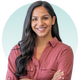 A woman in a red shirt is smiling with her arms crossed.