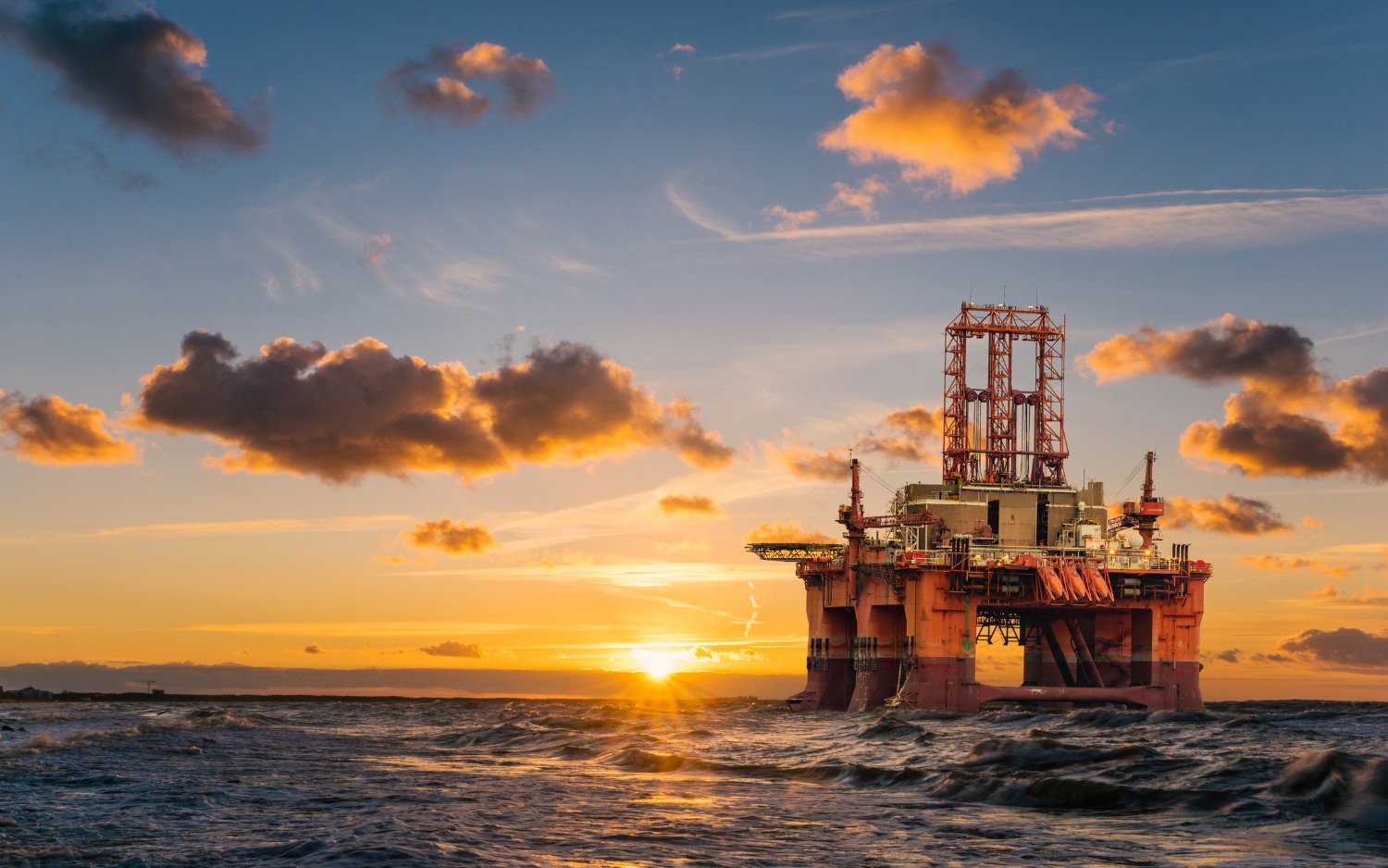An oil rig in the middle of the ocean at sunset.