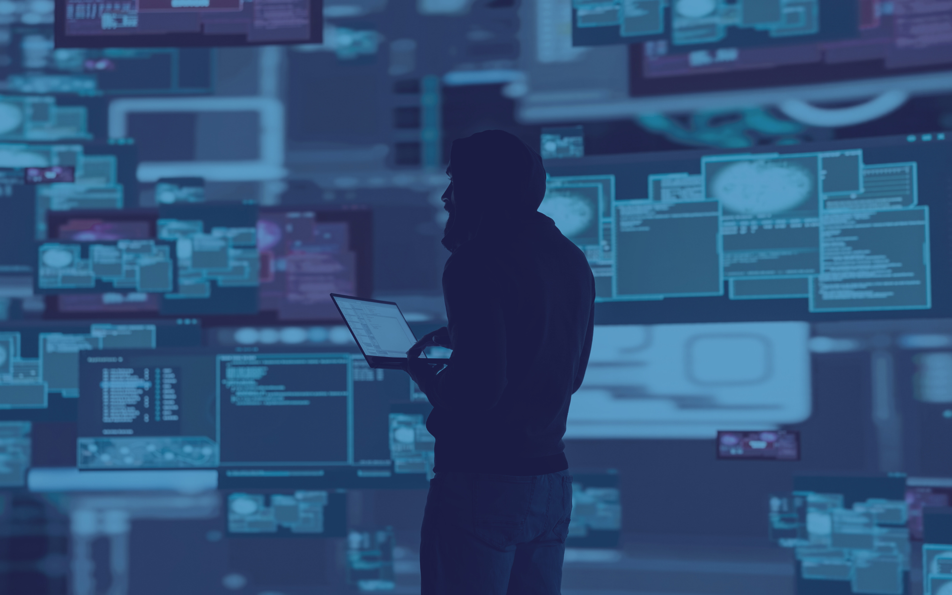 Silhouette of person holding laptop, surrounded by multiple glowing computer screens displaying code. Blue tones.