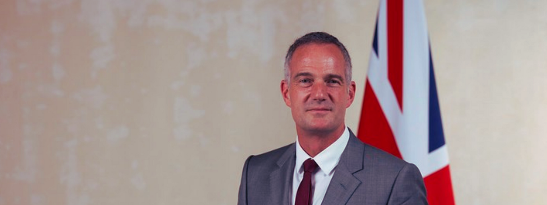 A man in a suit and tie is standing in front of a british flag.