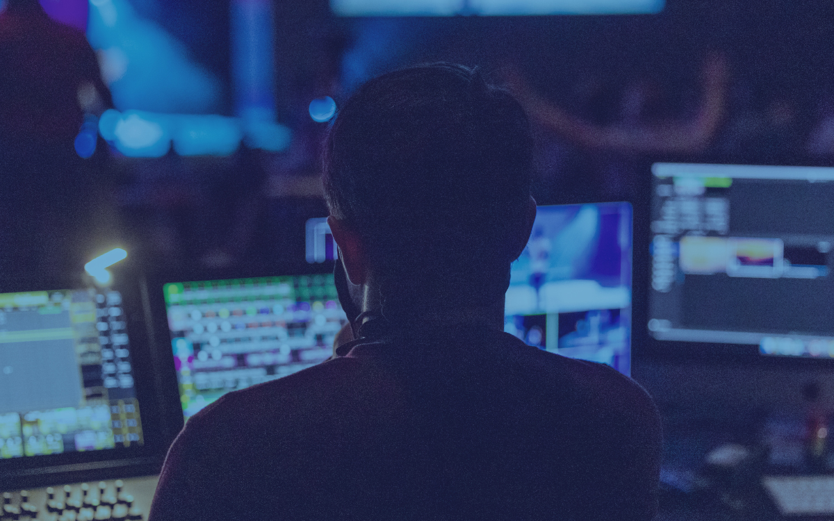 A man is sitting in front of a computer screen in a dark room.