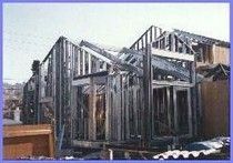 House frame under construction, exterior view with wood studs and open windows.