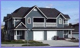 Two-story blue house with white trim, black roof, and two-car garage. Balcony with white railing.