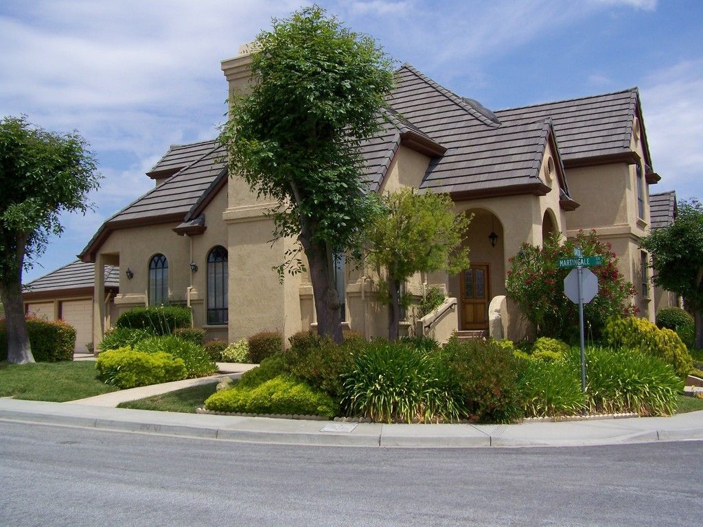 Tan stucco house with brown roof and landscaping.