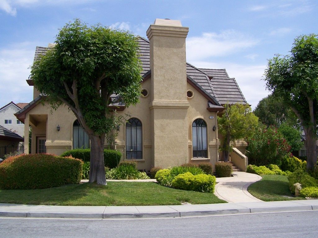 Beige house with a tiled roof, arched windows, and a chimney, with a curved pathway and green landscaping.
