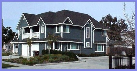 Two-story, blue house with white trim, dark roof, and two-car garage. Landscaping and a black fence.