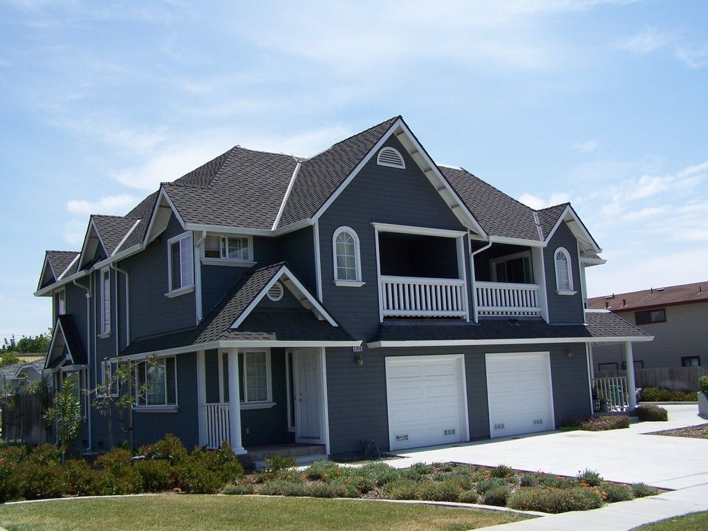 Two-story blue house with white trim, two-car garage, and balconies under a bright sky.