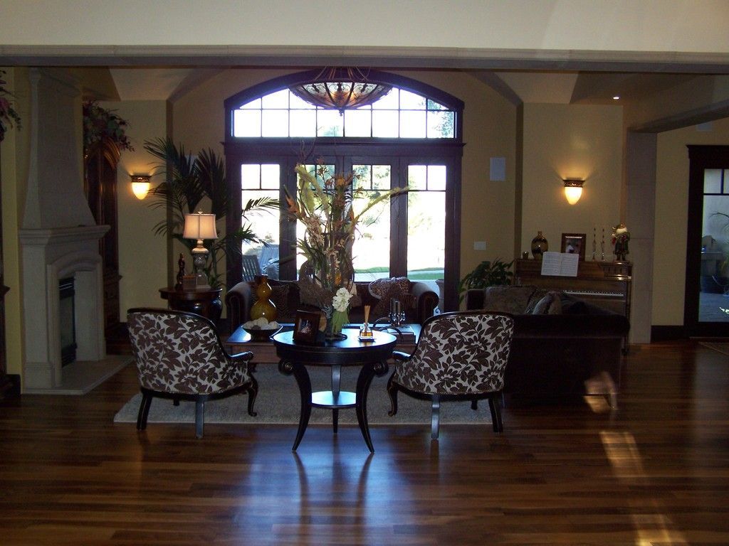 Living room with hardwood floors, two patterned chairs, table, and a large arched window with a view.