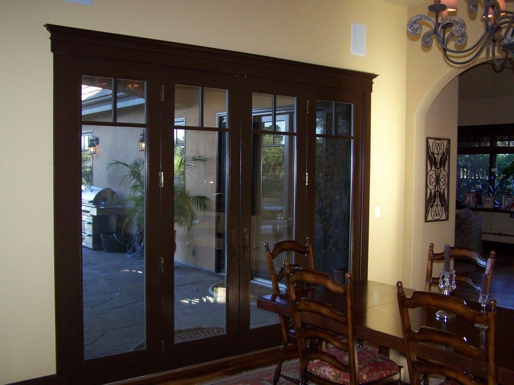 Dark wood framed doors with glass panes, leading to an outdoor patio, are open in a dining room.