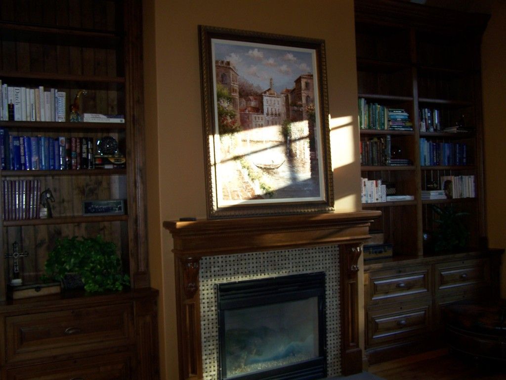 Fireplace with painting, flanked by bookshelves, in a room with warm lighting.