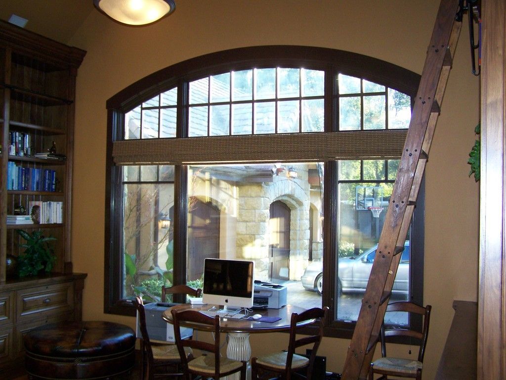 Two-story beige stucco house with a three-car garage, wet driveway, and manicured lawn under a cloudy sky.
