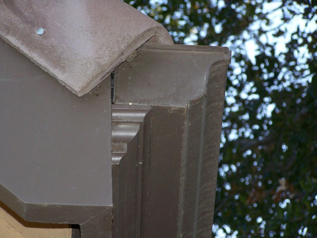 Copper gutter and downspout on a building's corner. Dark brown trim and beige stucco.