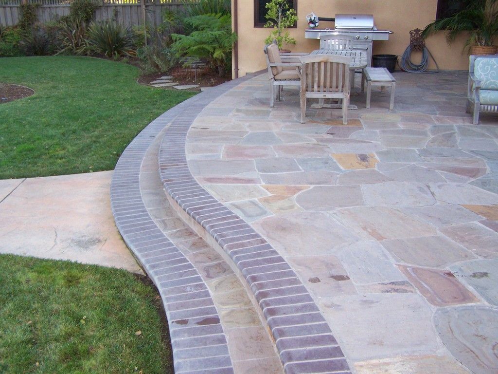 Elegant home entryway with arched wooden door, wreath, topiary trees, and stone steps.