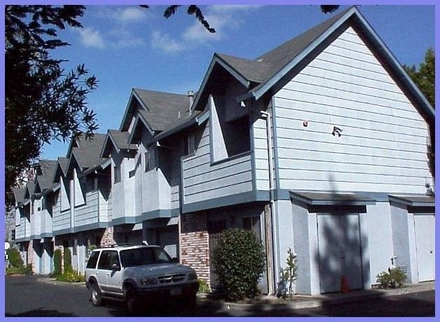 Row of light blue townhouses with gray gabled roofs; parked SUV.