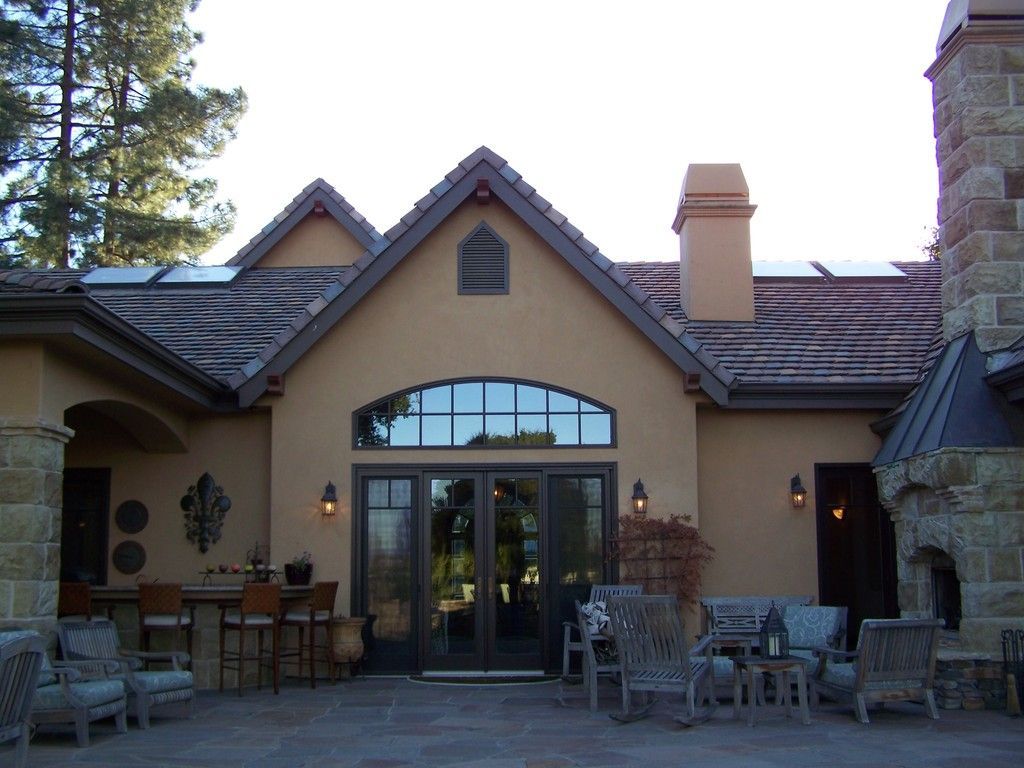 Tan stucco home with arched window, glass doors, and outdoor seating on a patio.