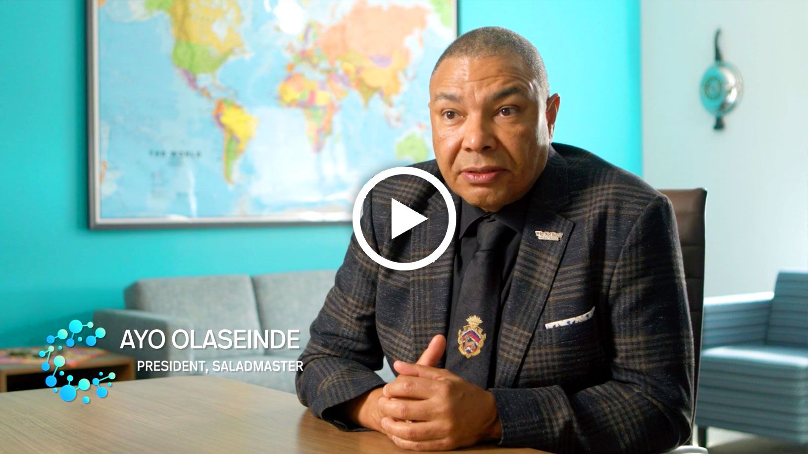 Man in suit speaking, world map backdrop.