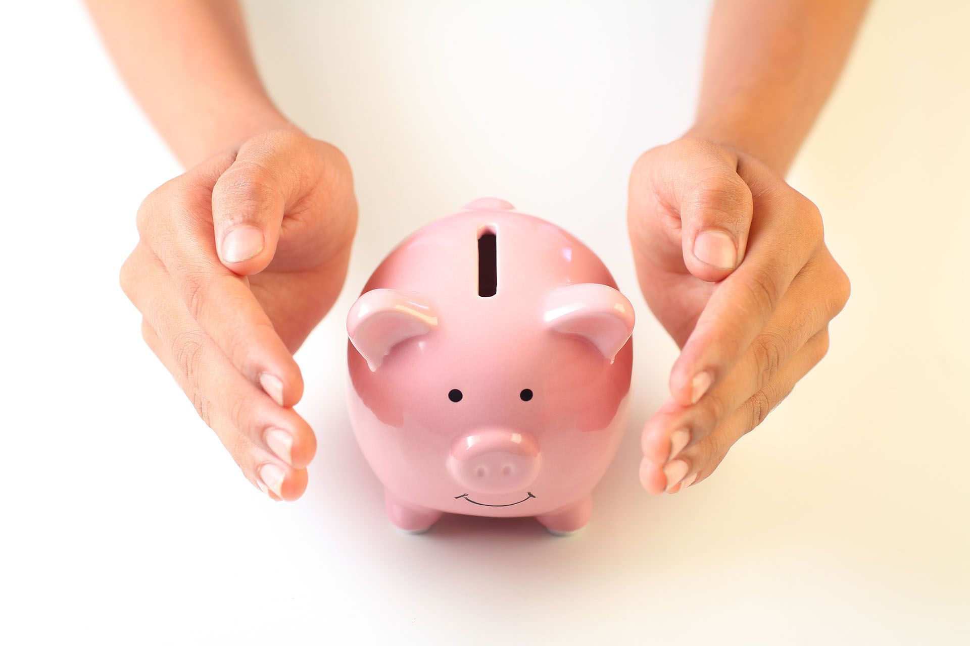 Hands cupping a pink piggy bank on a white surface, suggesting financial security or savings.