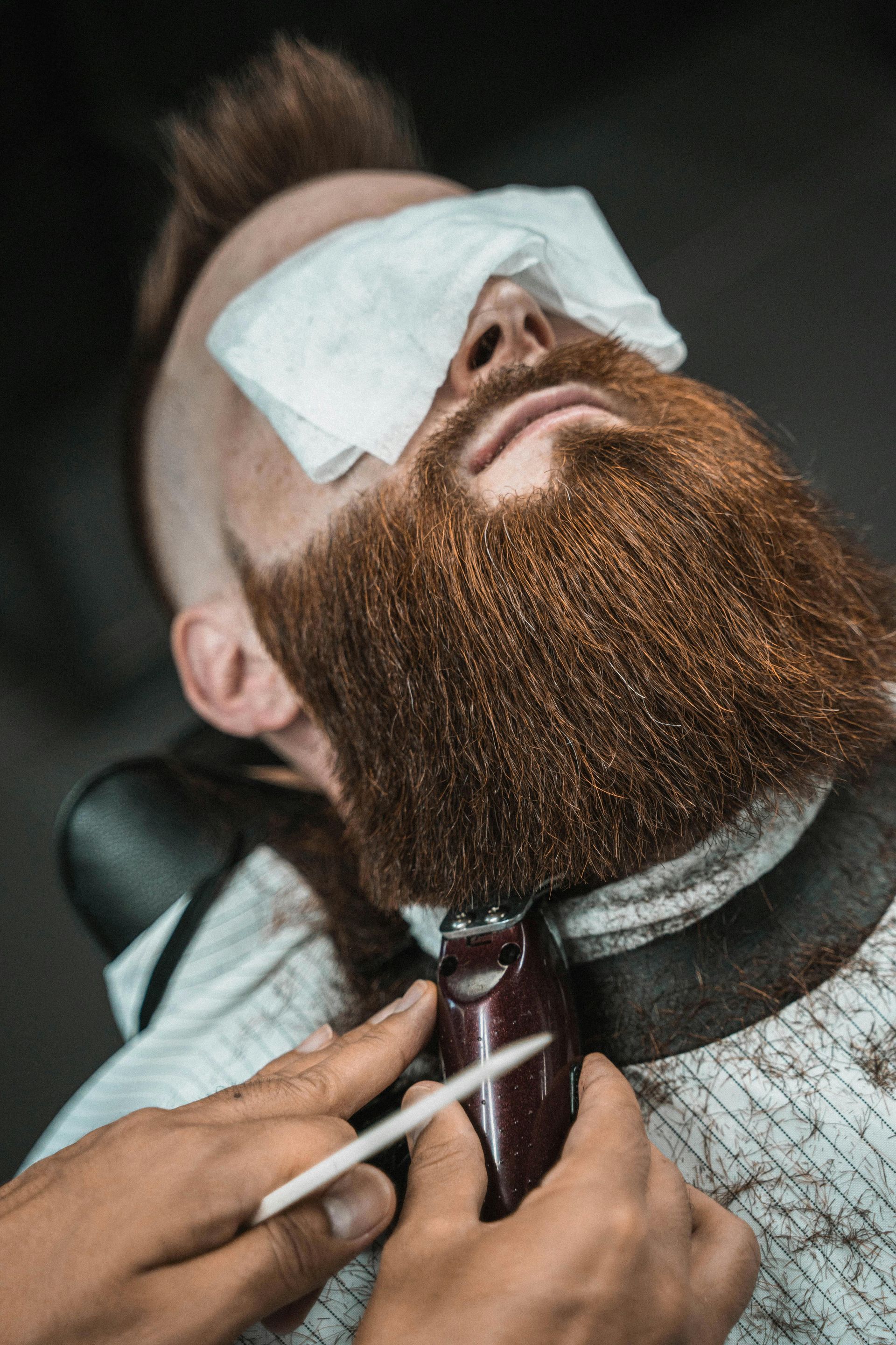 Person getting beard trimmed at a barber shop, eyes covered with a cloth.