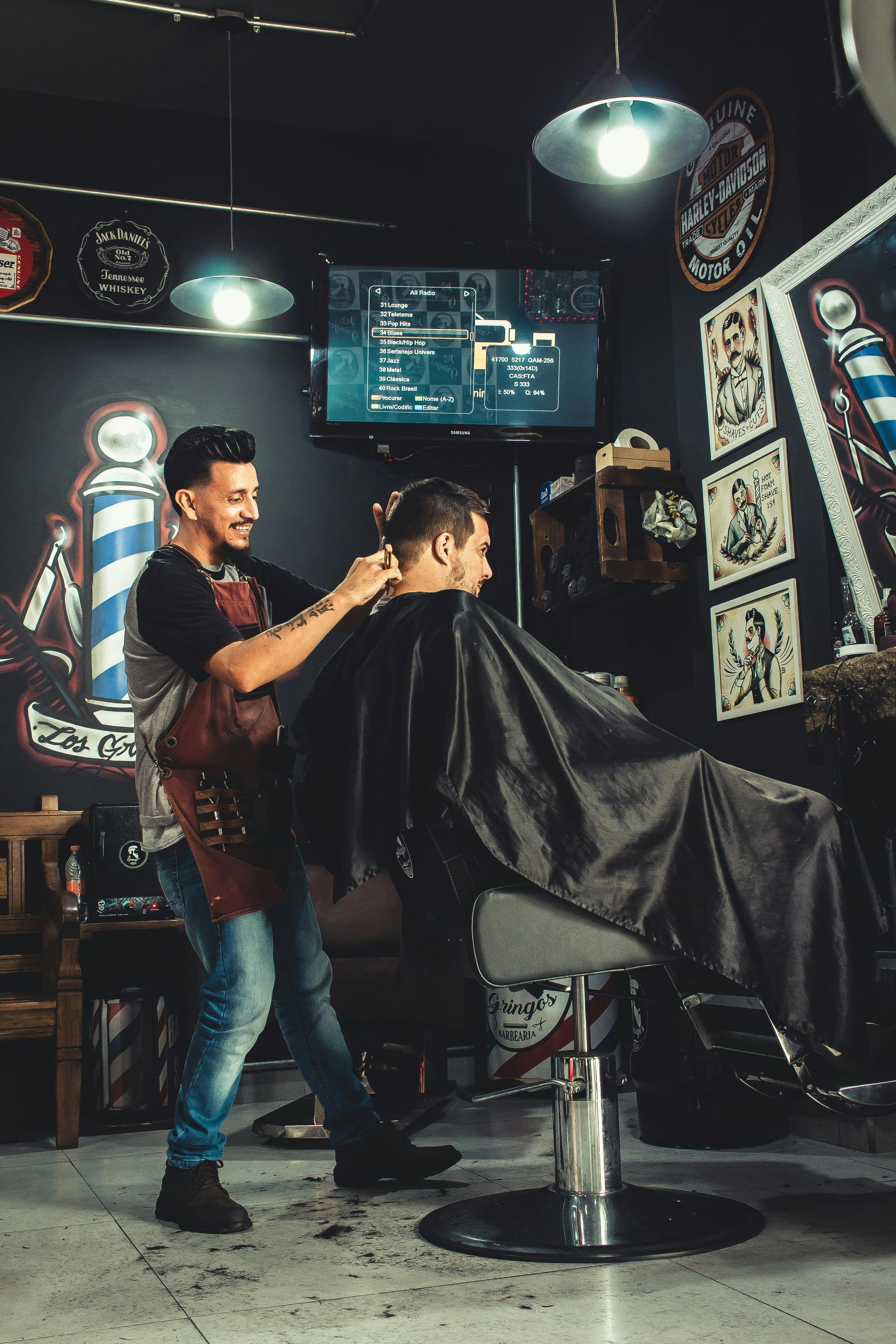 Barber giving a haircut in a barbershop; black walls with neon lights; man in chair.