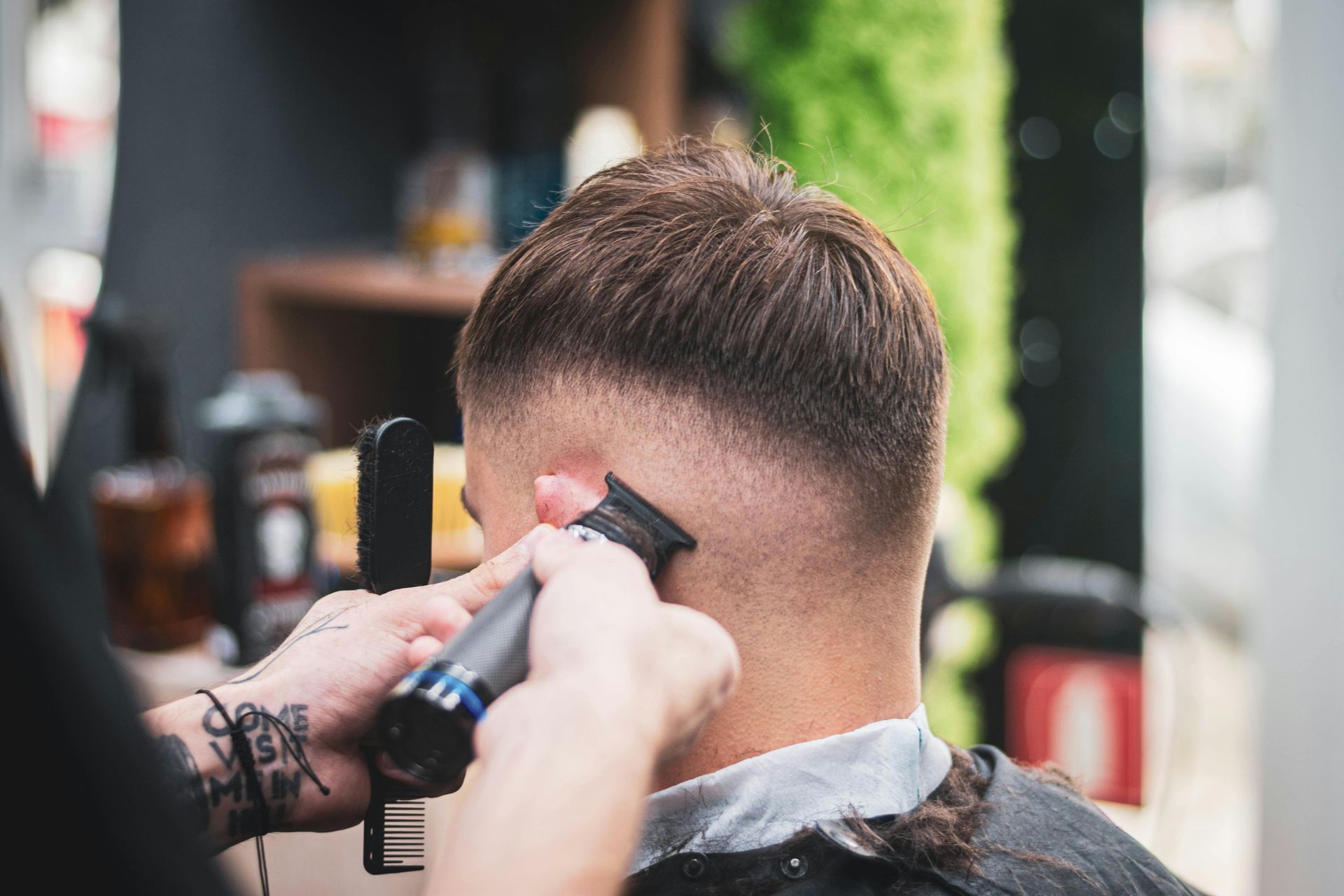 Barber giving a fade haircut with clippers, focusing on the back of the head.