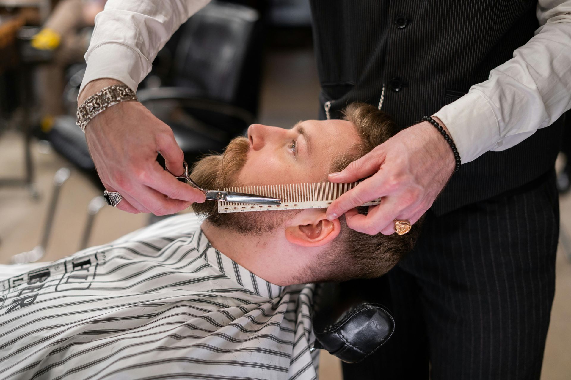 Barber trimming a man's beard with a straight razor and a beard comb in a barbershop.