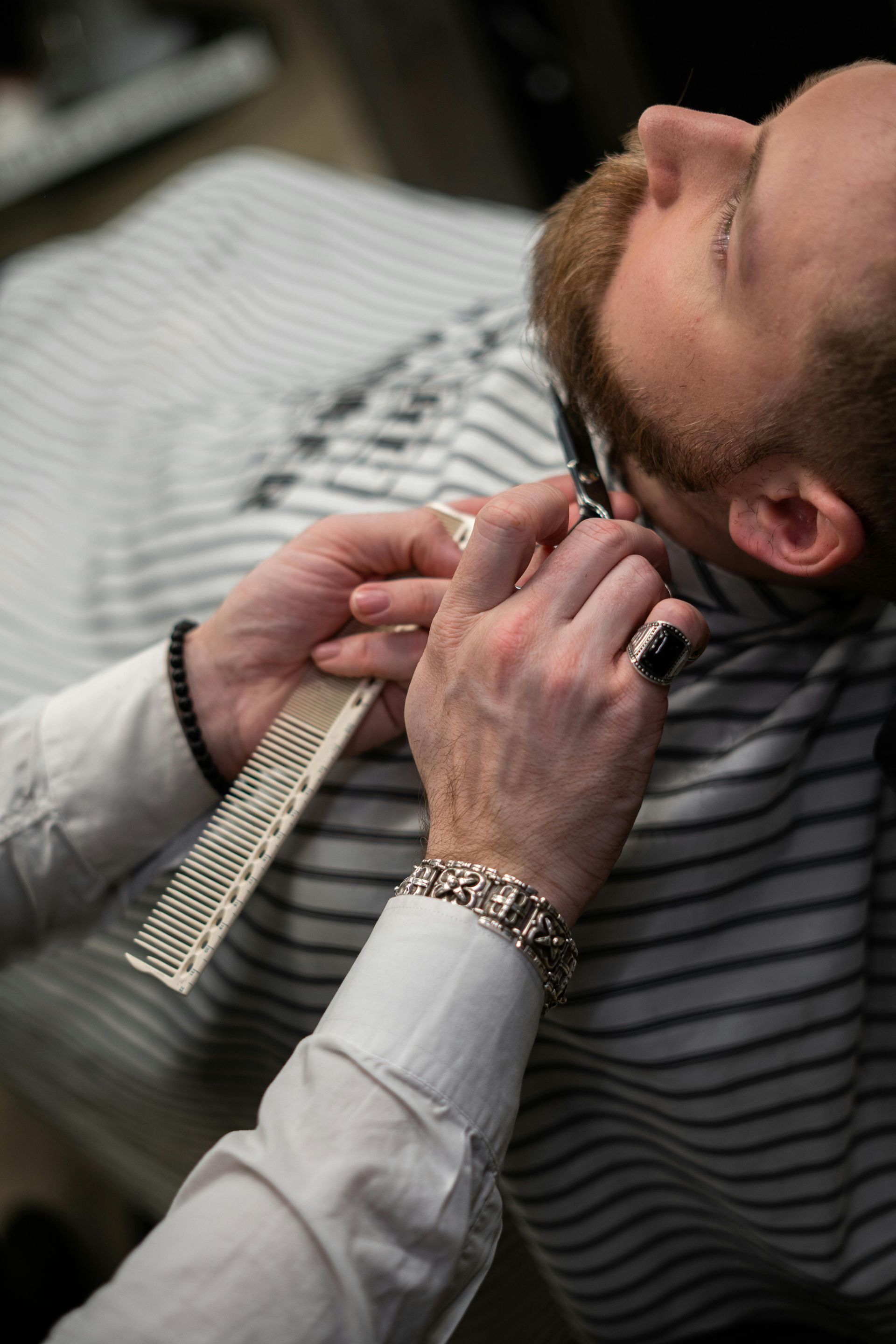 Barber trimming a customer's beard with a straight razor and comb in a barber shop.