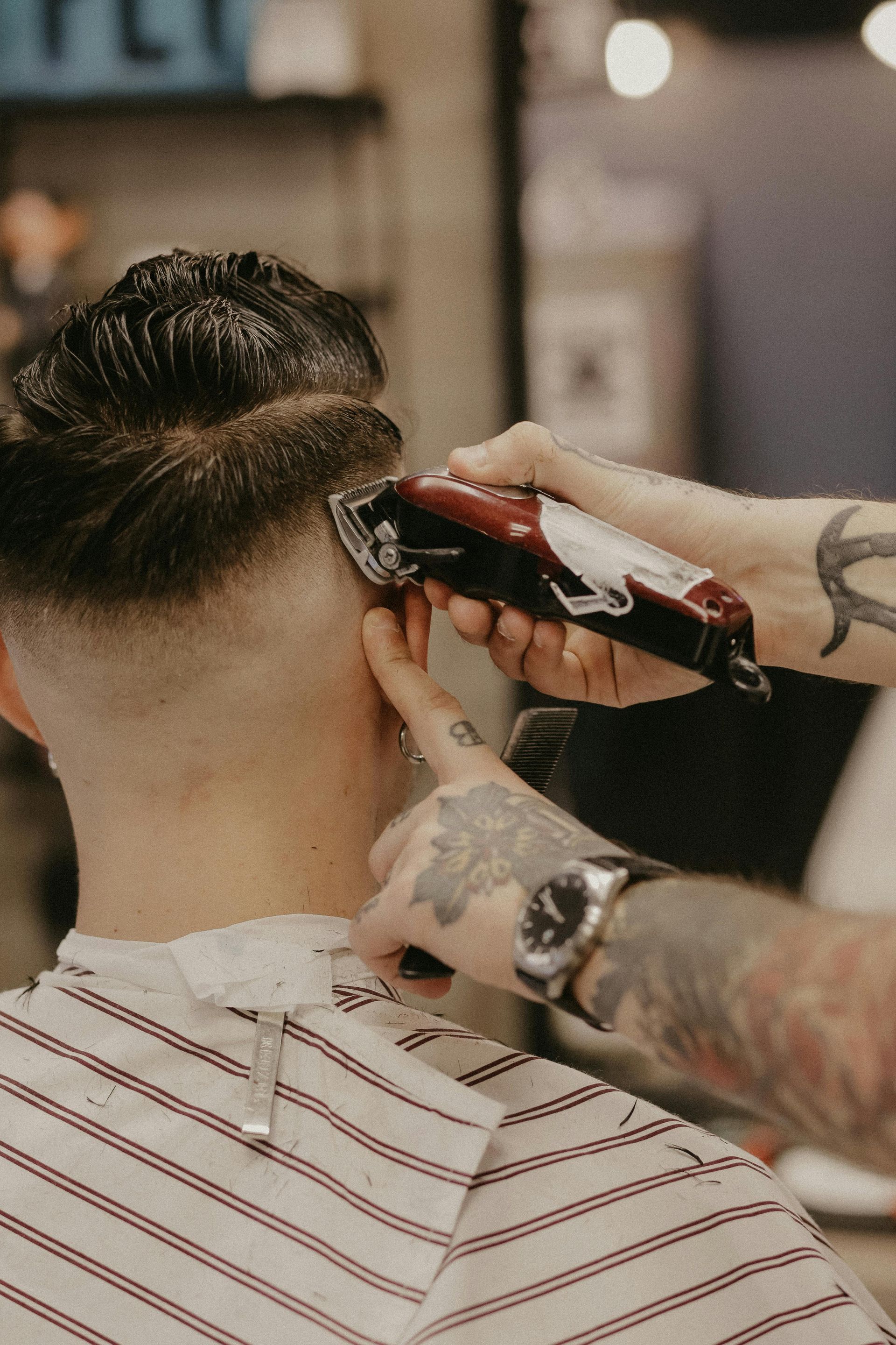 A barber using clippers to cut a client's hair in a barbershop.