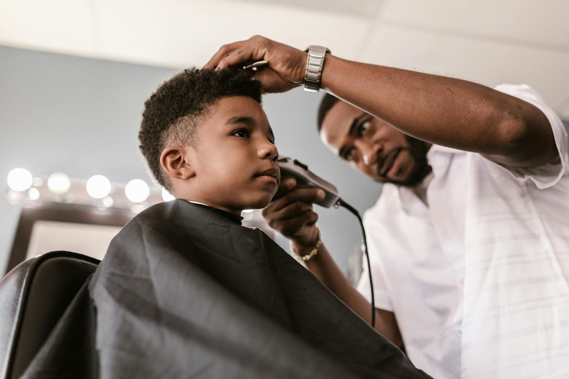 Barber giving a young boy a haircut with electric clippers in a salon.